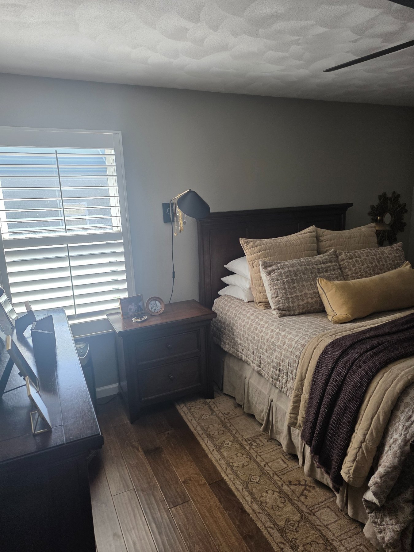 Bedroom with dark wood furniture, cream patterned bedding, a plum throw, and a gold cushion.