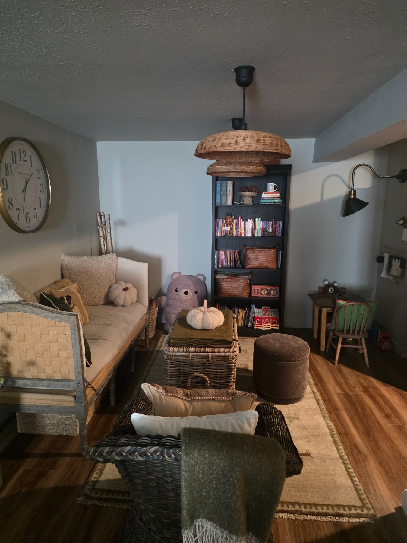 Small reading area with a woven daybed, wicker trunk, baskets, bookcase, and pendant lights.