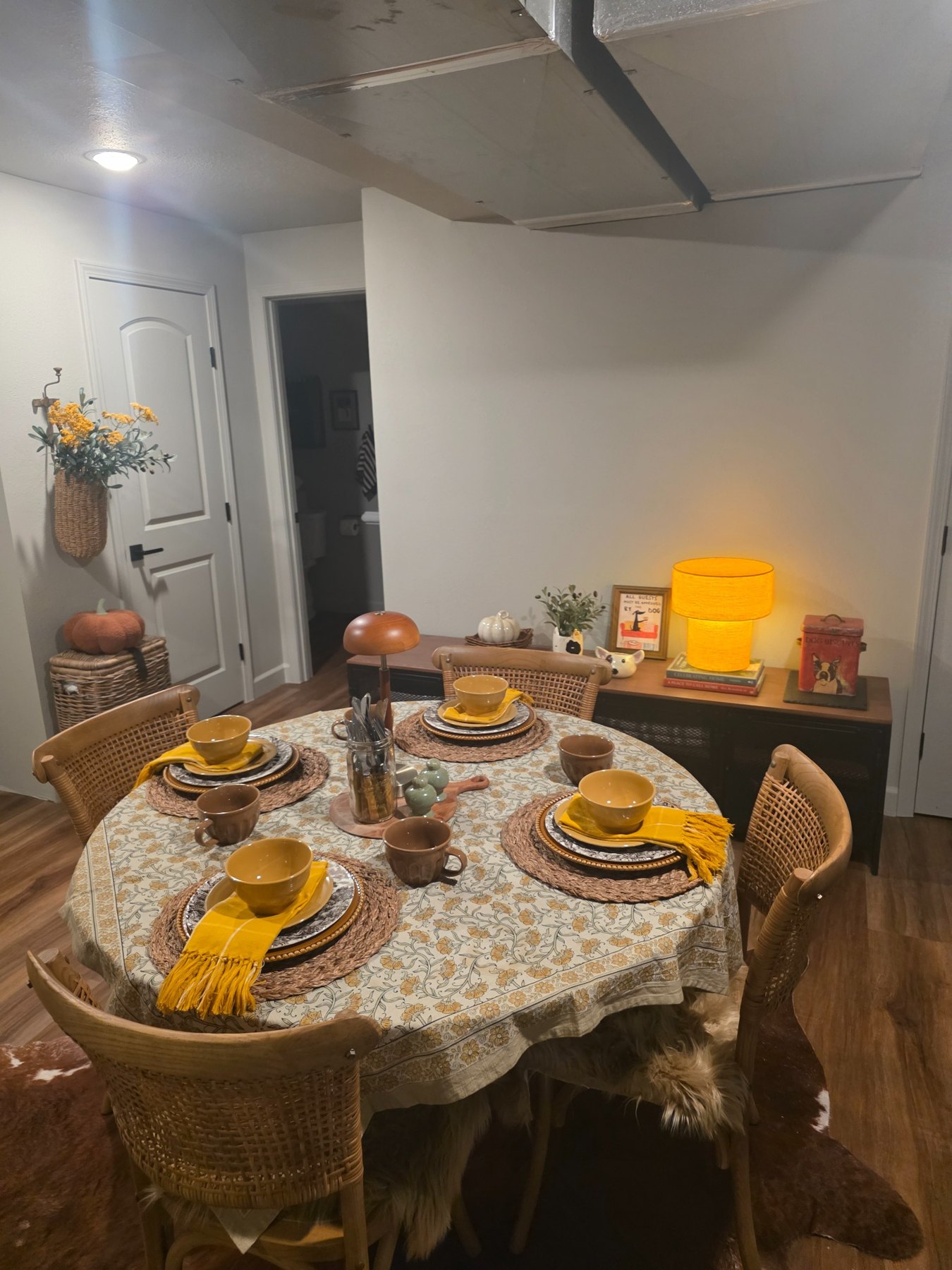 Round table set with mustard napkins, yellow bowls, woven placemats, and a patterned cloth.